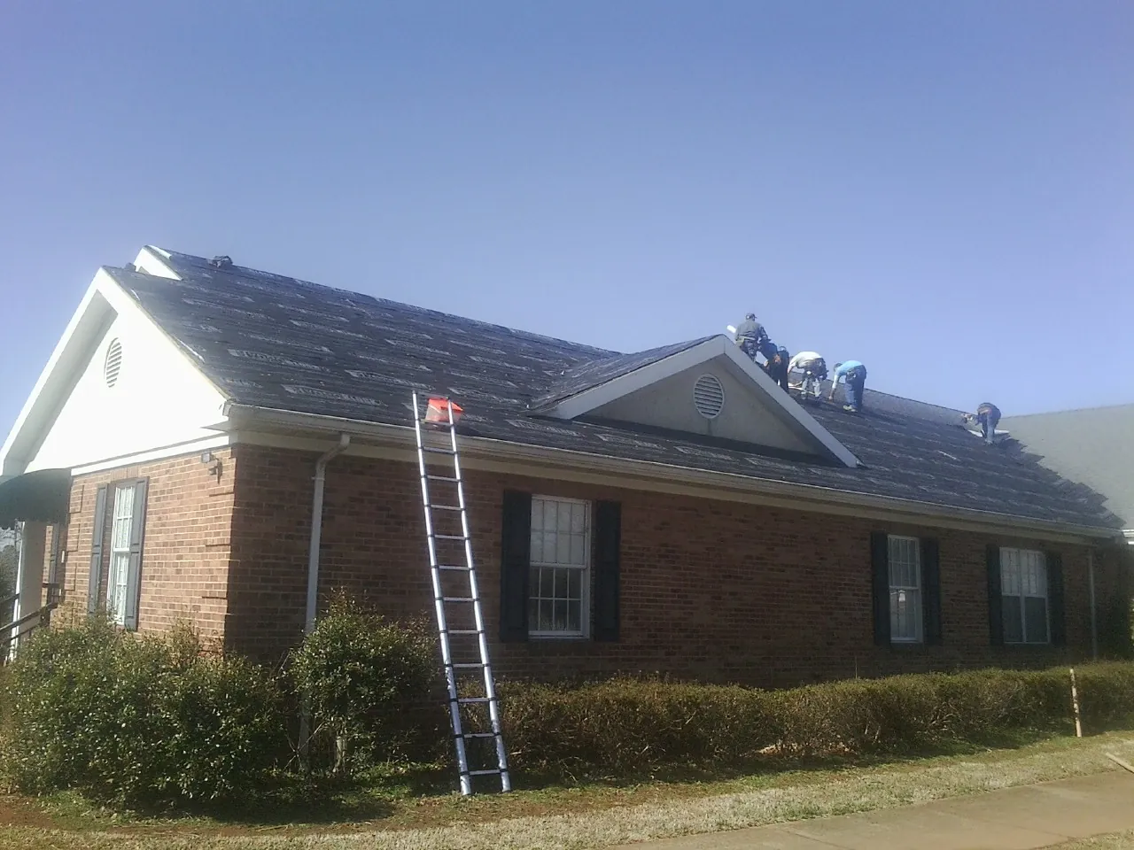 Crew tearing shingles off a brick ranch roof with a ladder set — Metal Roof Repair work by our crew in Ashford