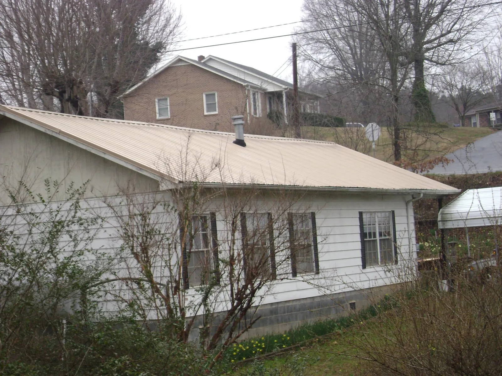 Tan metal roof on a white sided house set into a hillside — Commercial Roofing by Roofing Brothers in Ashford